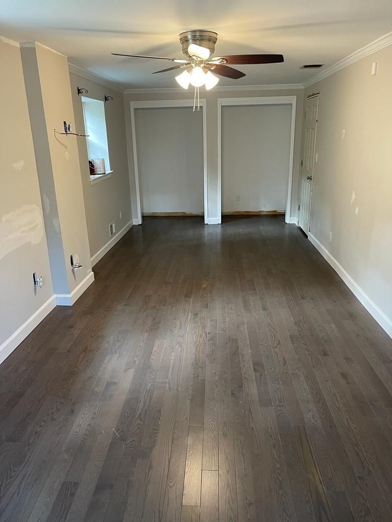 Empty room with dark hardwood floors, beige walls, and a ceiling fan.