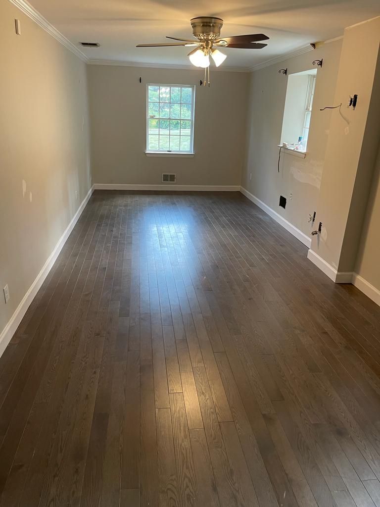 Empty room with wood floors, a window, and a ceiling fan. Walls are painted light beige.
