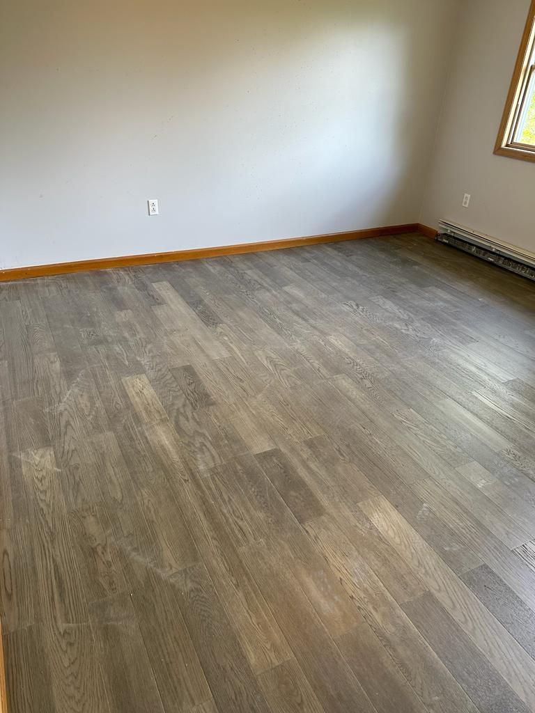 Empty room with gray-stained hardwood floors, light gray walls, and a small window.