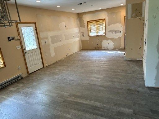 Empty room under construction with new gray flooring, patched walls, and doorway.