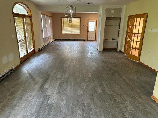 A room with grey wood-look flooring, beige walls, and various doors and windows.