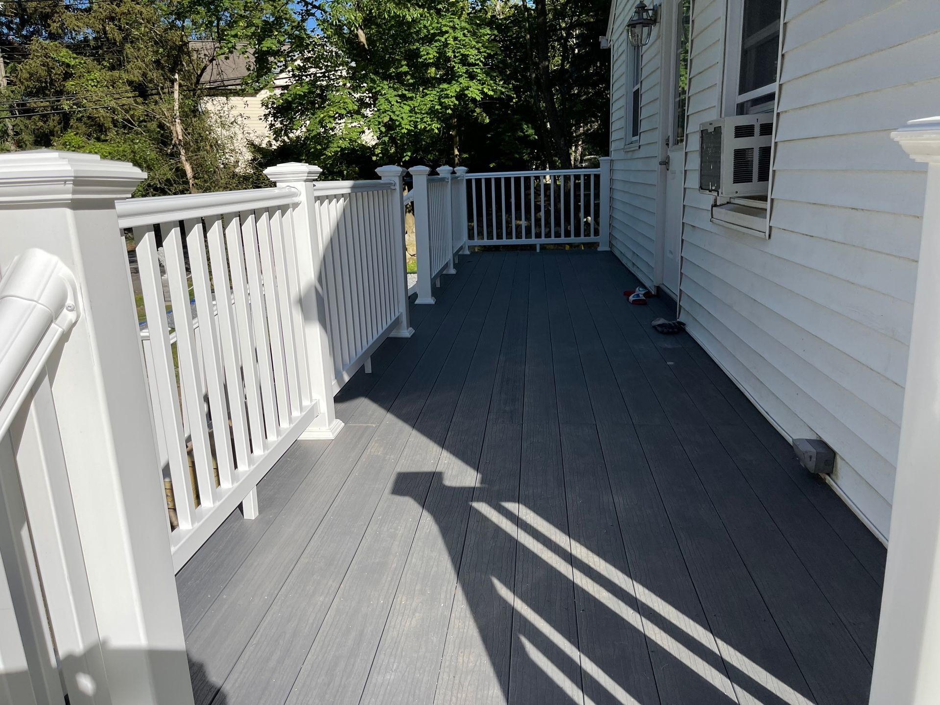 Gray deck with white railings on a white house, surrounded by trees.