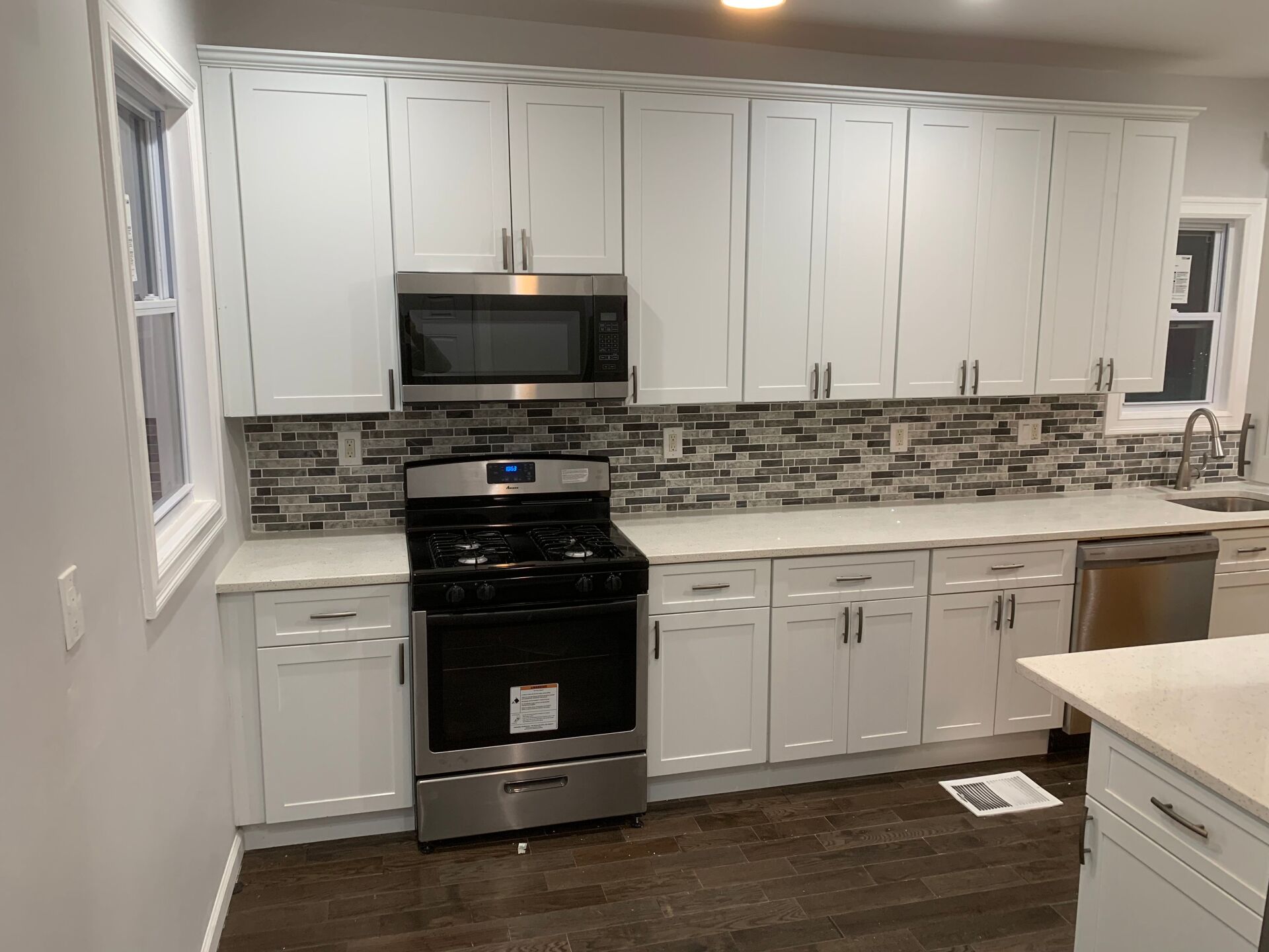 White kitchen cabinets with stainless steel appliances, backsplash, and dark wood floors.