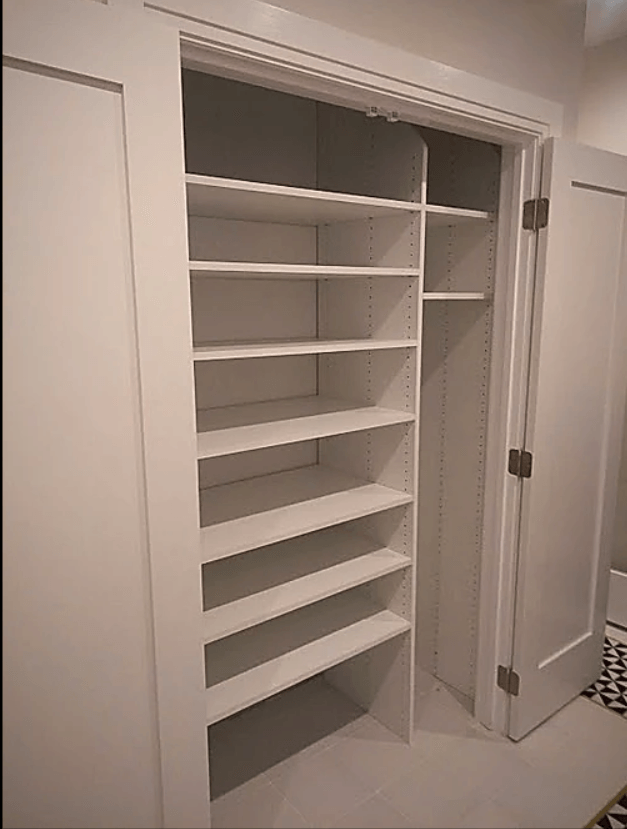 White shelving unit inside a closet with closed door on the right.