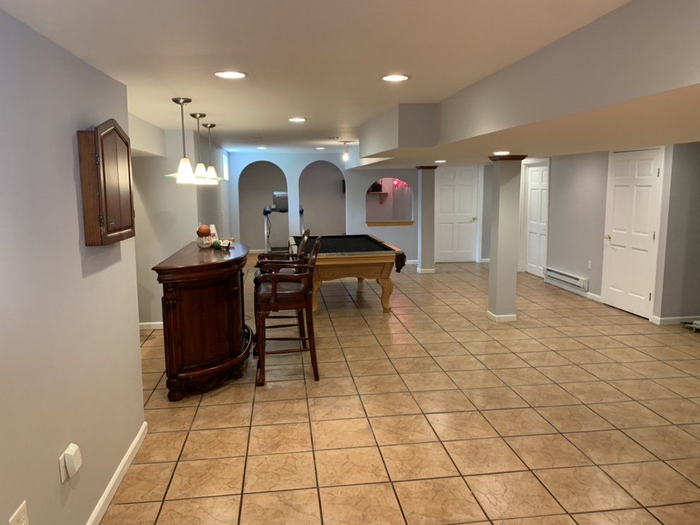Basement with bar, pool table, and tiled floor; light blue walls, brown cabinets.