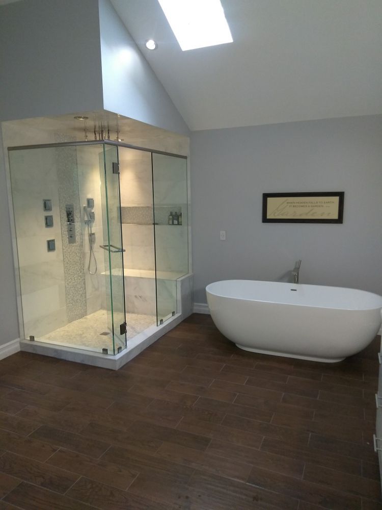 Modern bathroom with glass shower, freestanding tub, brown tile floor, and skylight.