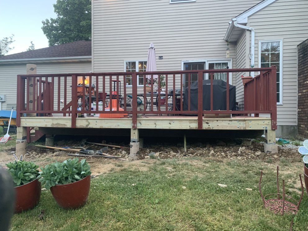 Wooden deck with reddish railing attached to a beige house, with debris visible below.