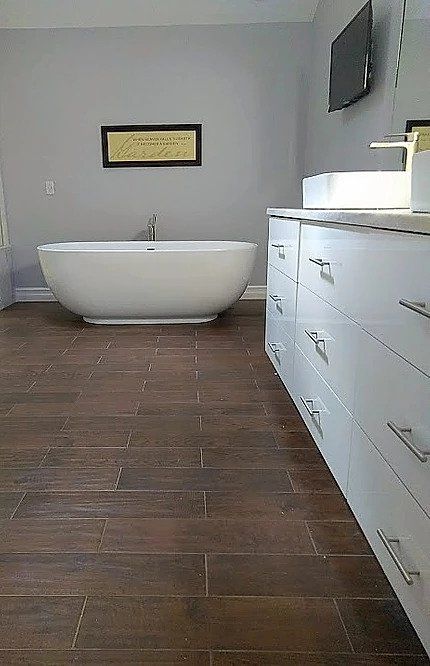 Modern bathroom with a white tub and vanity; brown tile floor and gray walls.