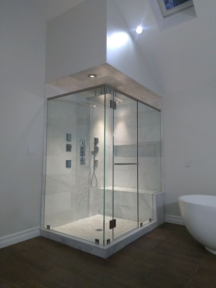 Corner glass shower in a modern bathroom, featuring a built-in bench and multiple shower heads.