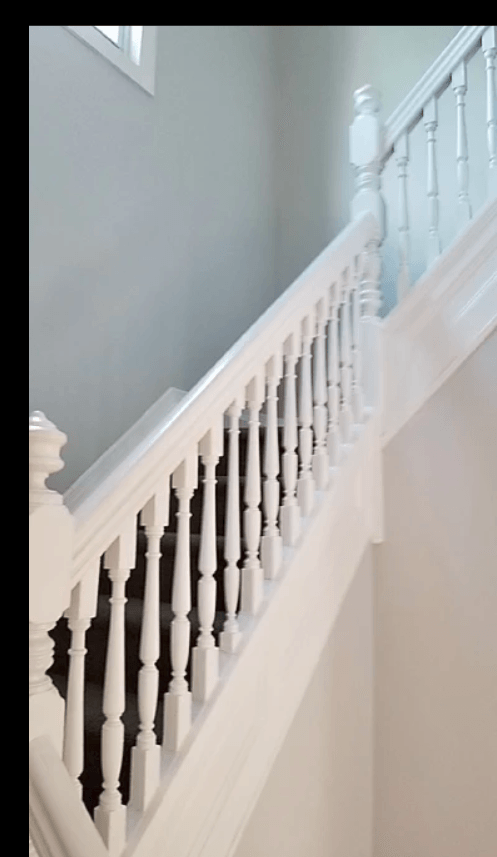White staircase with balusters and handrail, gray wall in background.