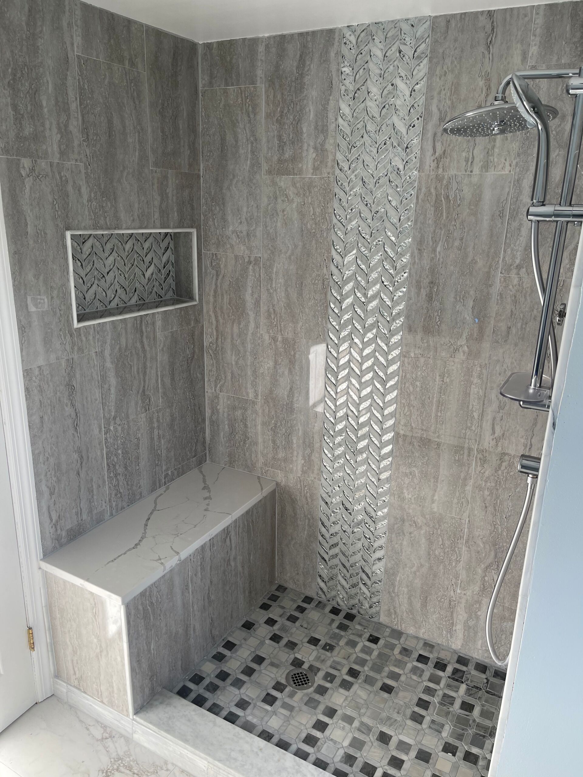 Gray tiled shower with bench, mosaic accent. Showerhead and niche.