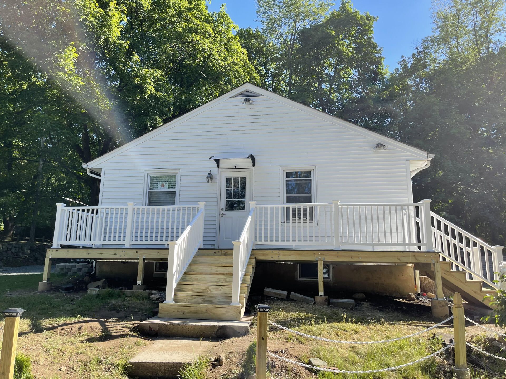 White house with deck and stairs, surrounded by trees.