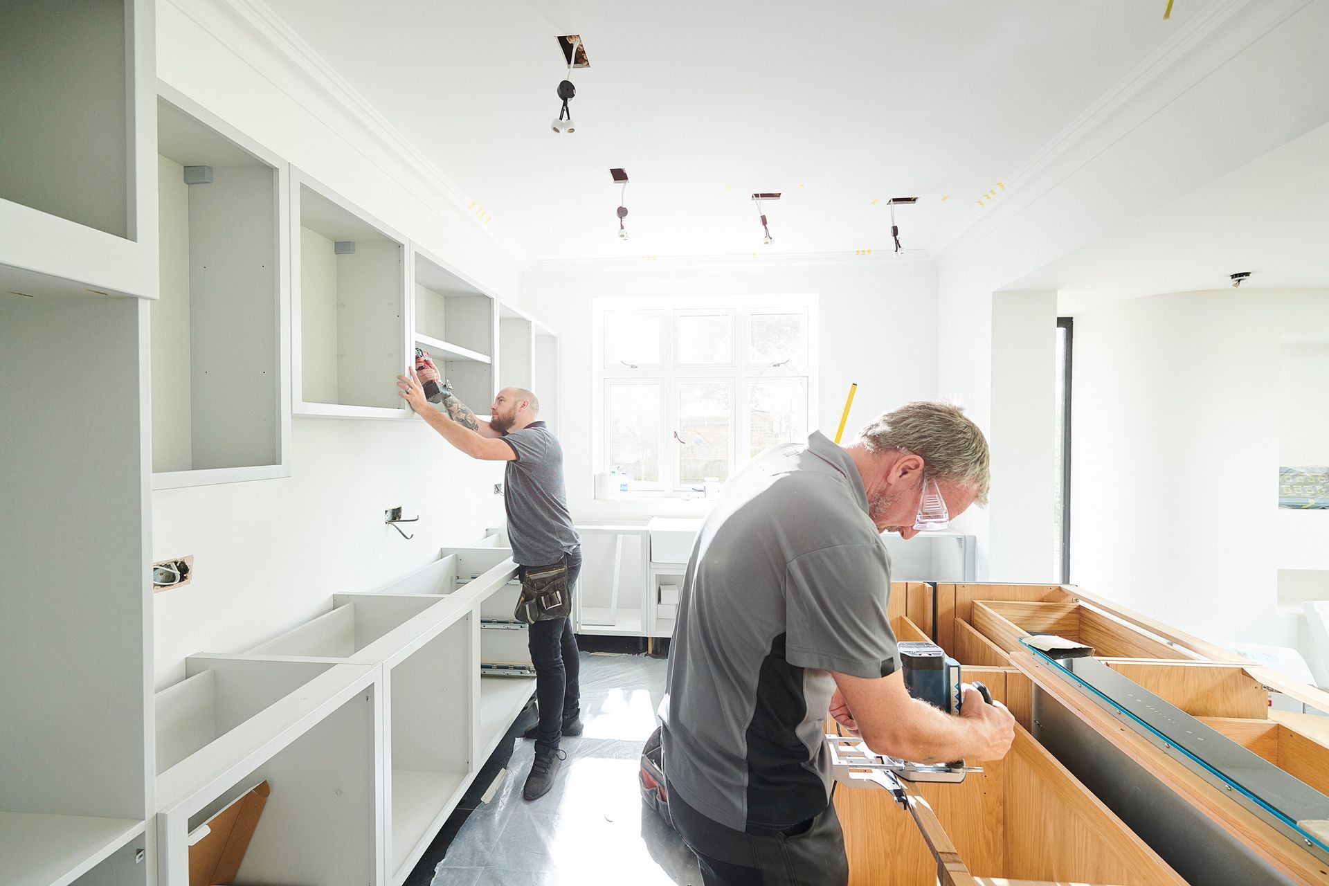 Two men are installing cabinets in a kitchen.