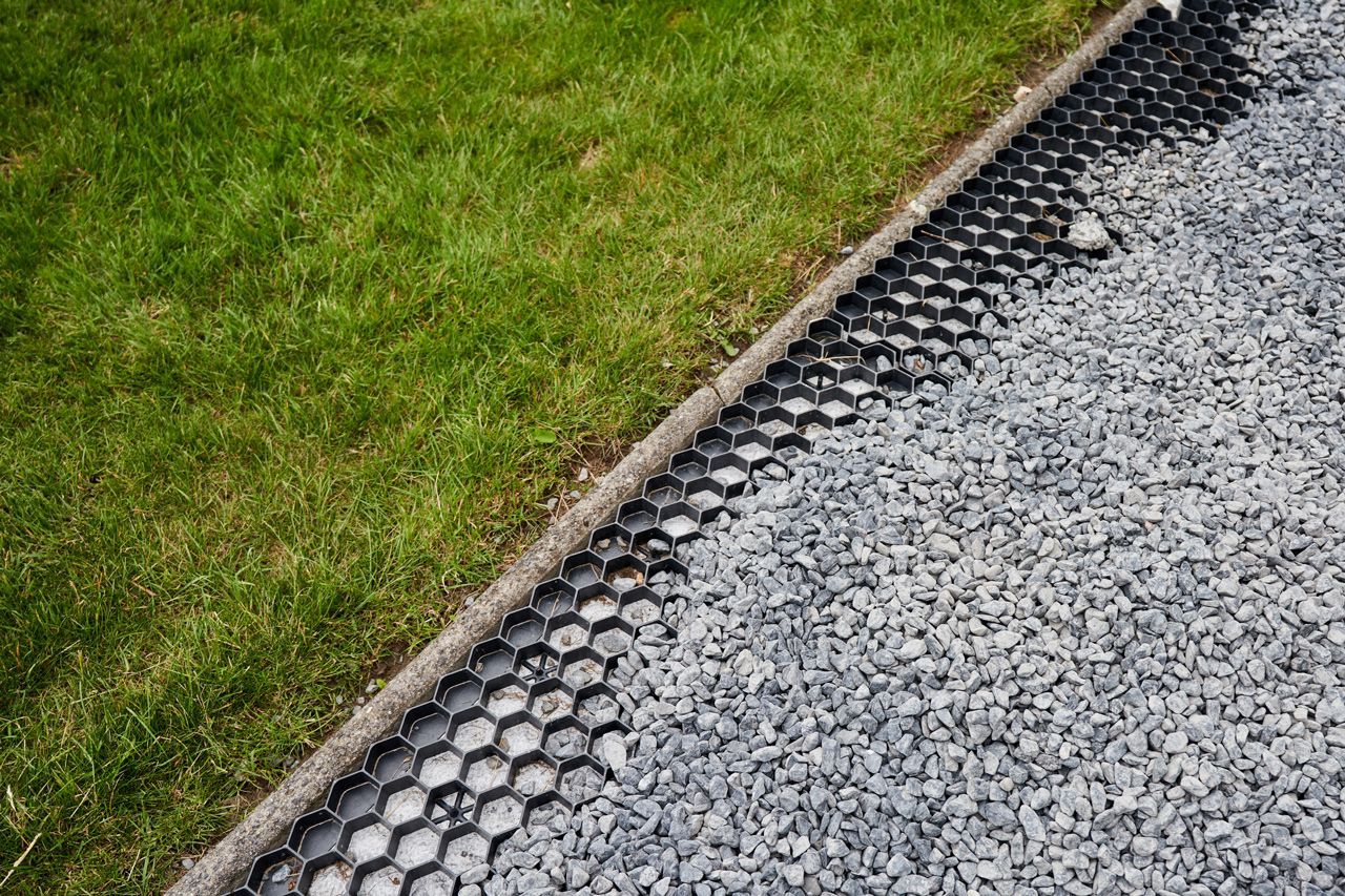 A gravel driveway next to a lush green lawn.