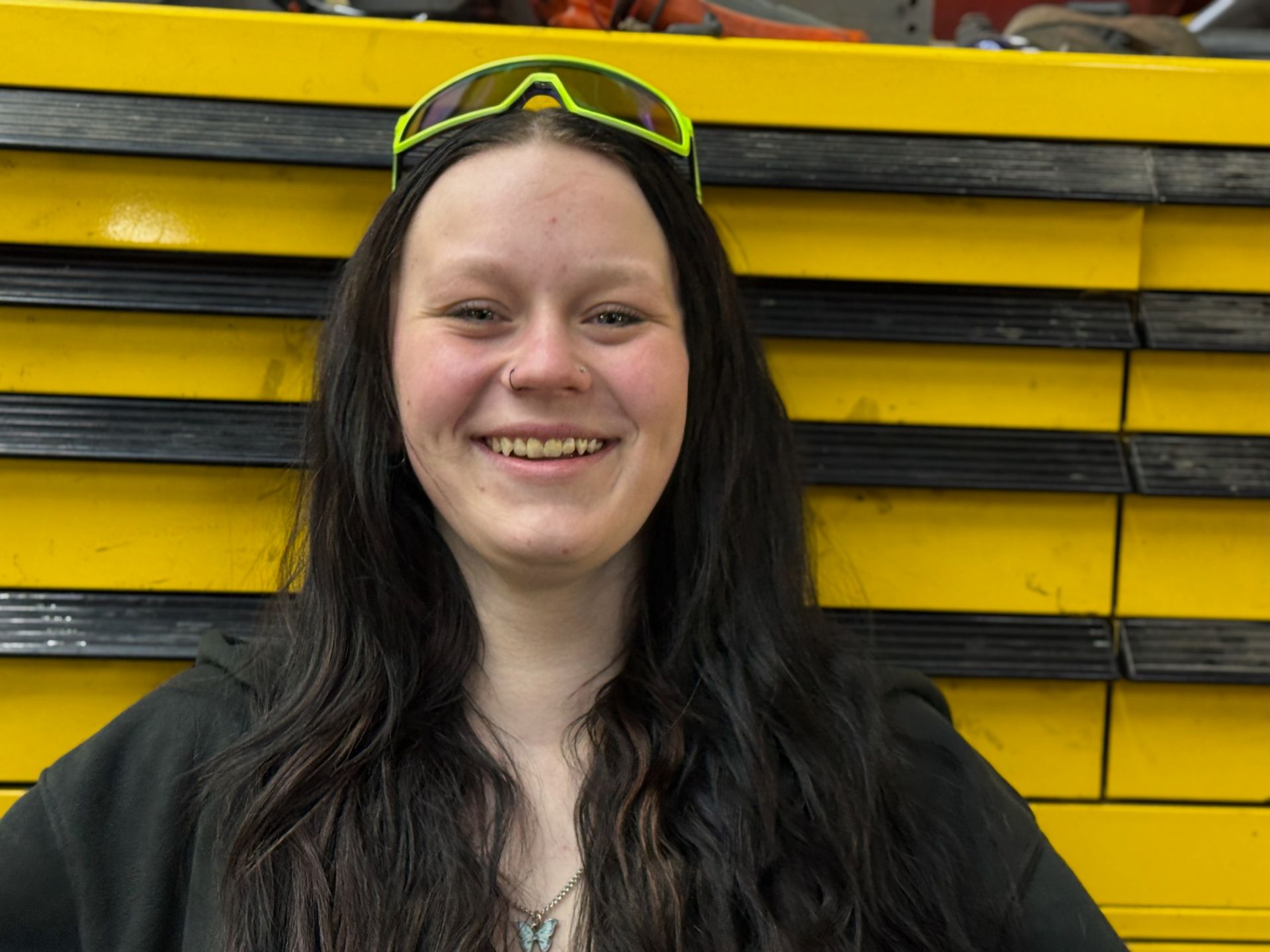 A woman wearing sunglasses is smiling in front of a yellow wall.