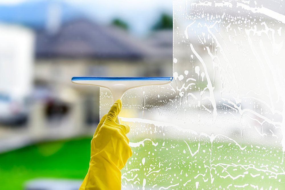 Cleaner Wearing Yellow Gloves Holding a Squeegee — Highlands Window Cleaning in Mittagong, NSW