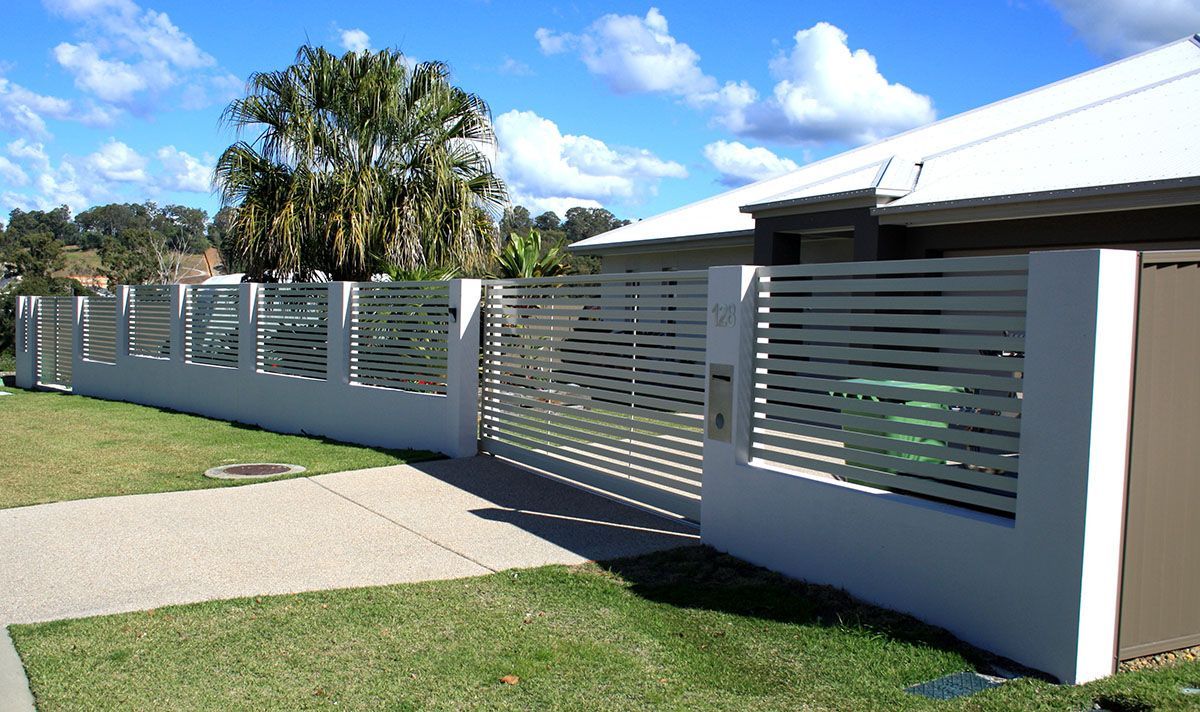 A white fence with a sliding gate in front of a house