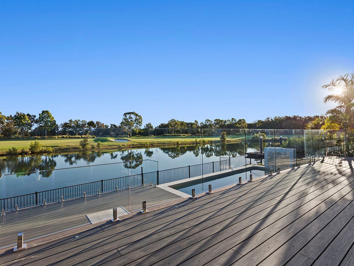A wooden deck overlooking a lake with a swimming pool and a golf course in the background.