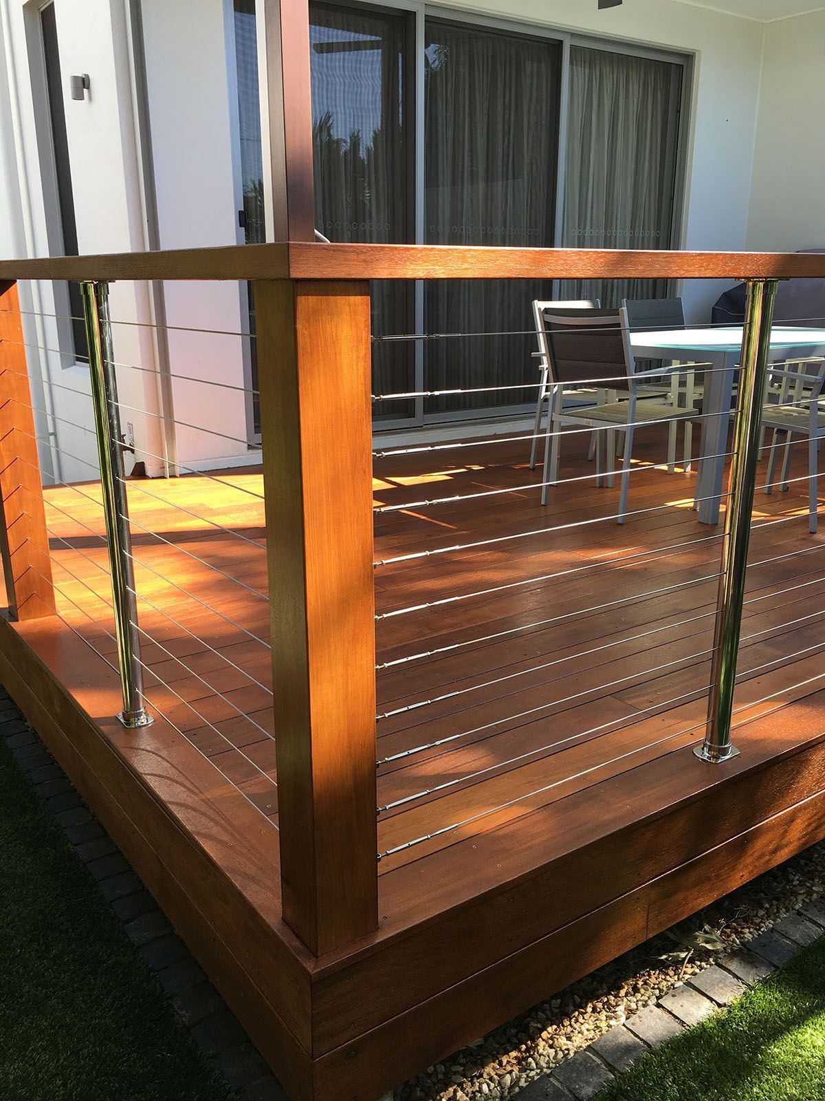 A wooden deck with a stainless steel railing and a table and chairs on it.