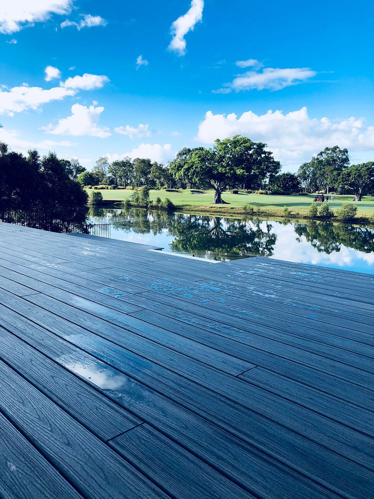 A wooden deck overlooking a lake with a golf course in the background.