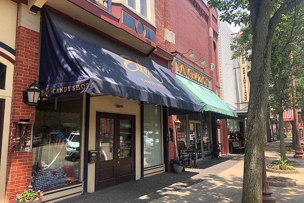 A street-level view of storefronts with awnings, including Eiler Candy Shop in Dover, under a bright sky with trees along the sidewalk.