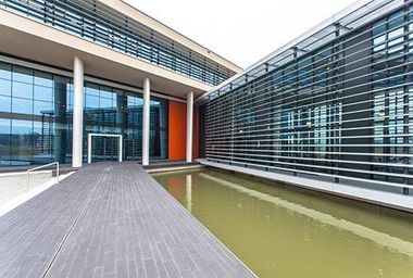 Modern building exterior with glass walls, water feature, and walkway.