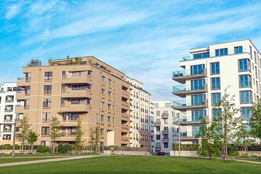 Modern apartment buildings with balconies against a blue sky, grassy lawn in foreground