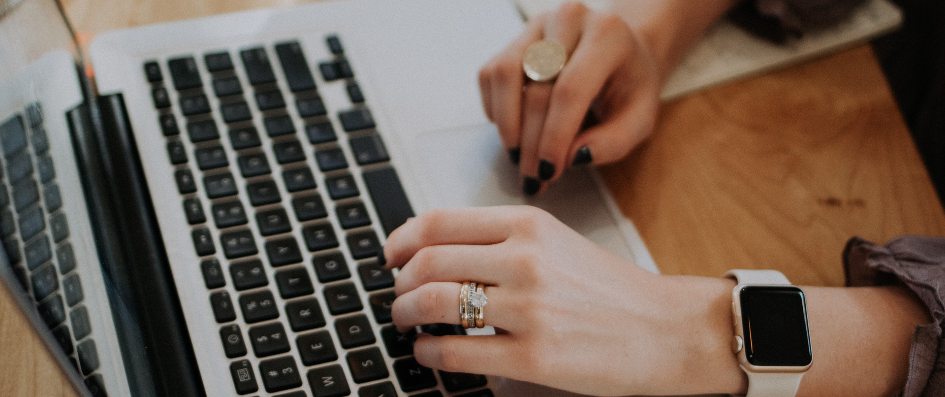 A woman typing on a laptop computer while wearing a watch and a ring.