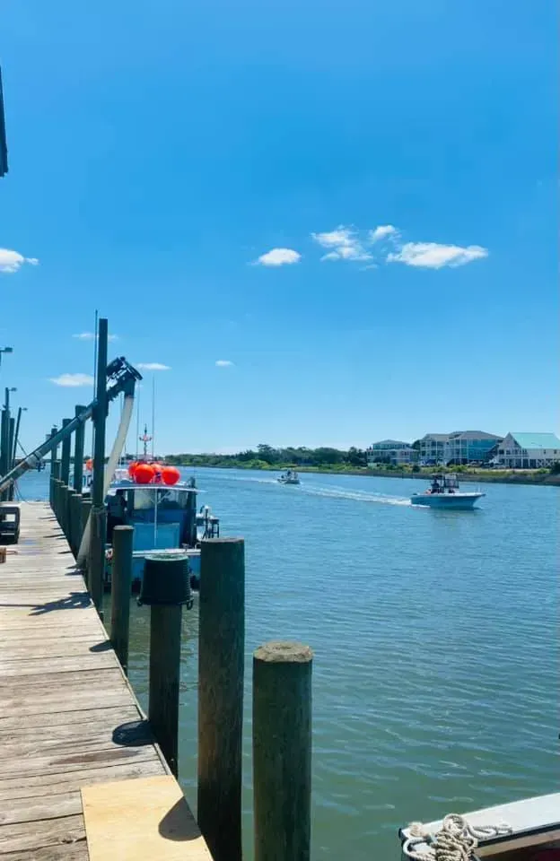 Wooden dock next to a waterway with boats sailing on a sunny day.