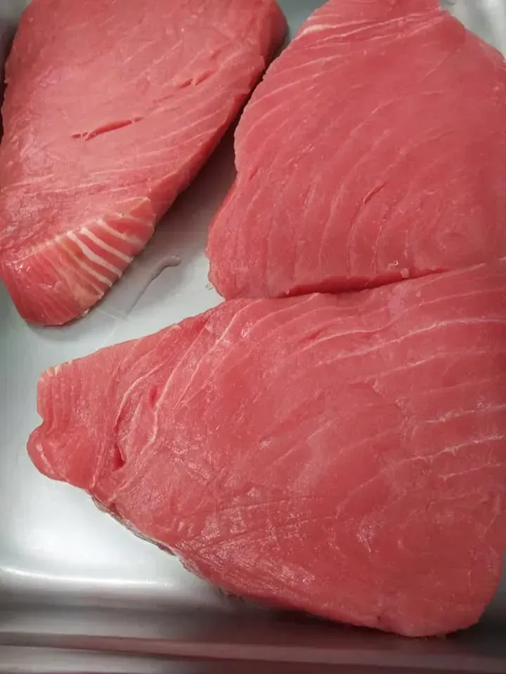Three raw, pink tuna steaks in a metal tray, ready for cooking.