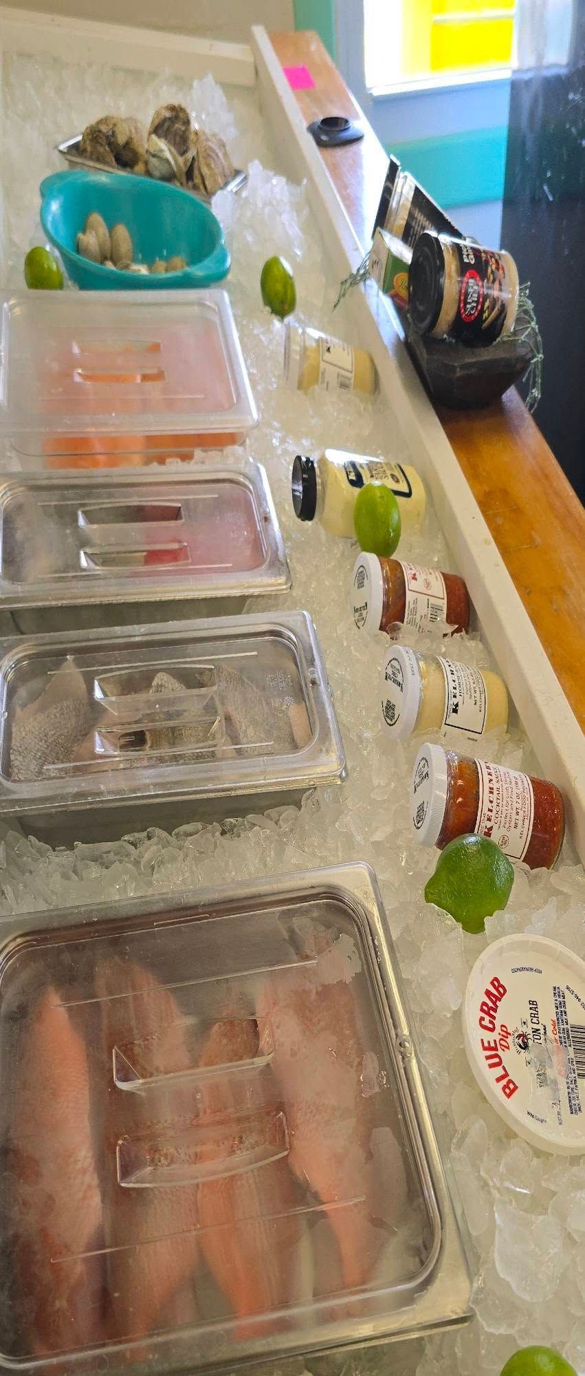 Seafood display on ice, including oysters, sushi, and fish fillets in clear containers.
