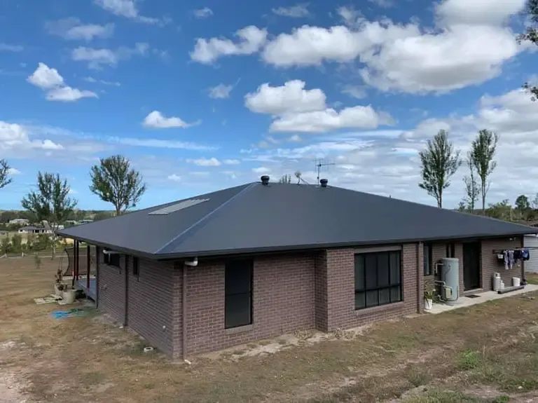 A Brick House With a Black Roof is Sitting in the Middle of a Field — Brett Negus Plumbing In Oakhurst, QLD