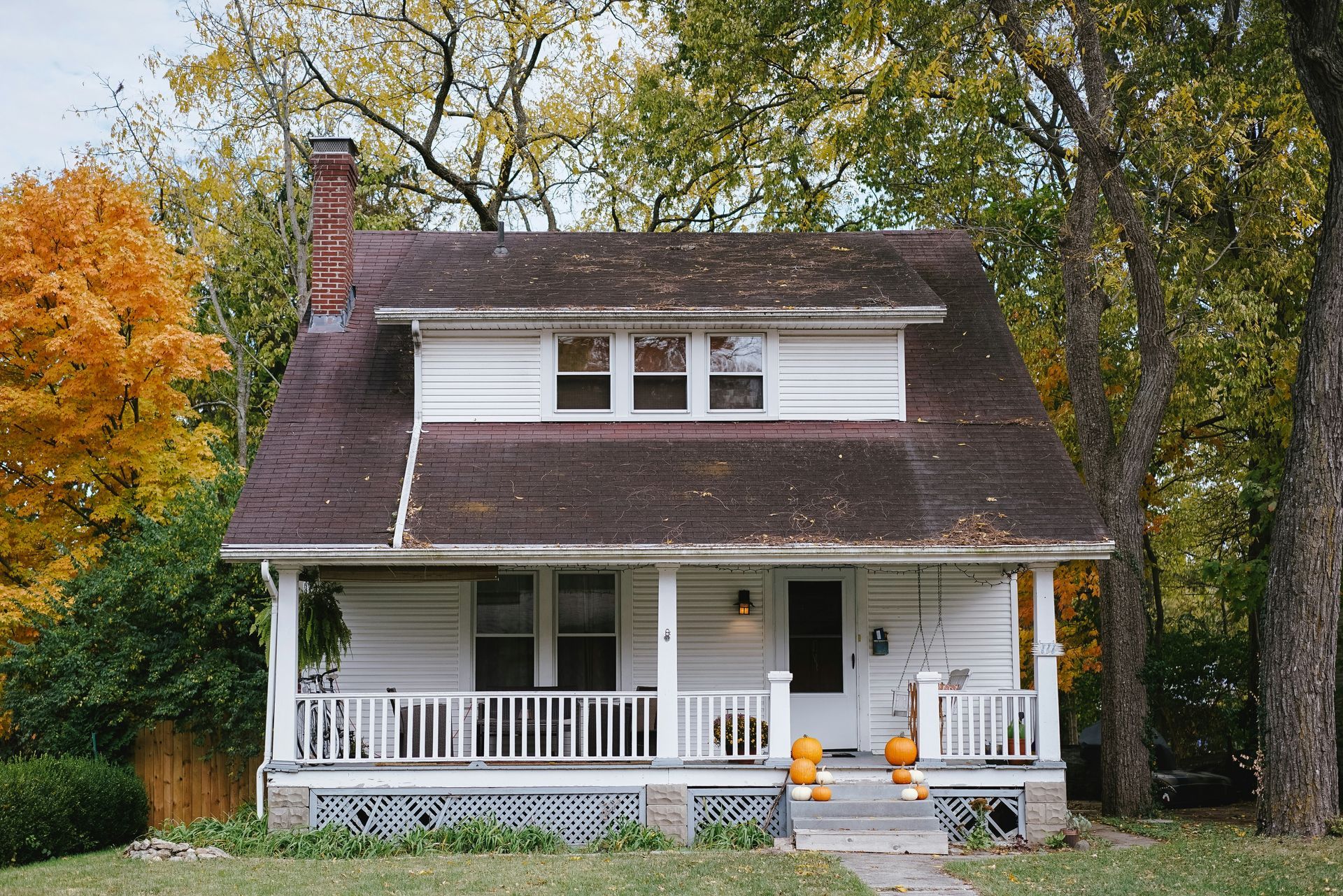 A white house with a brown roof and a porch decorated for halloween.