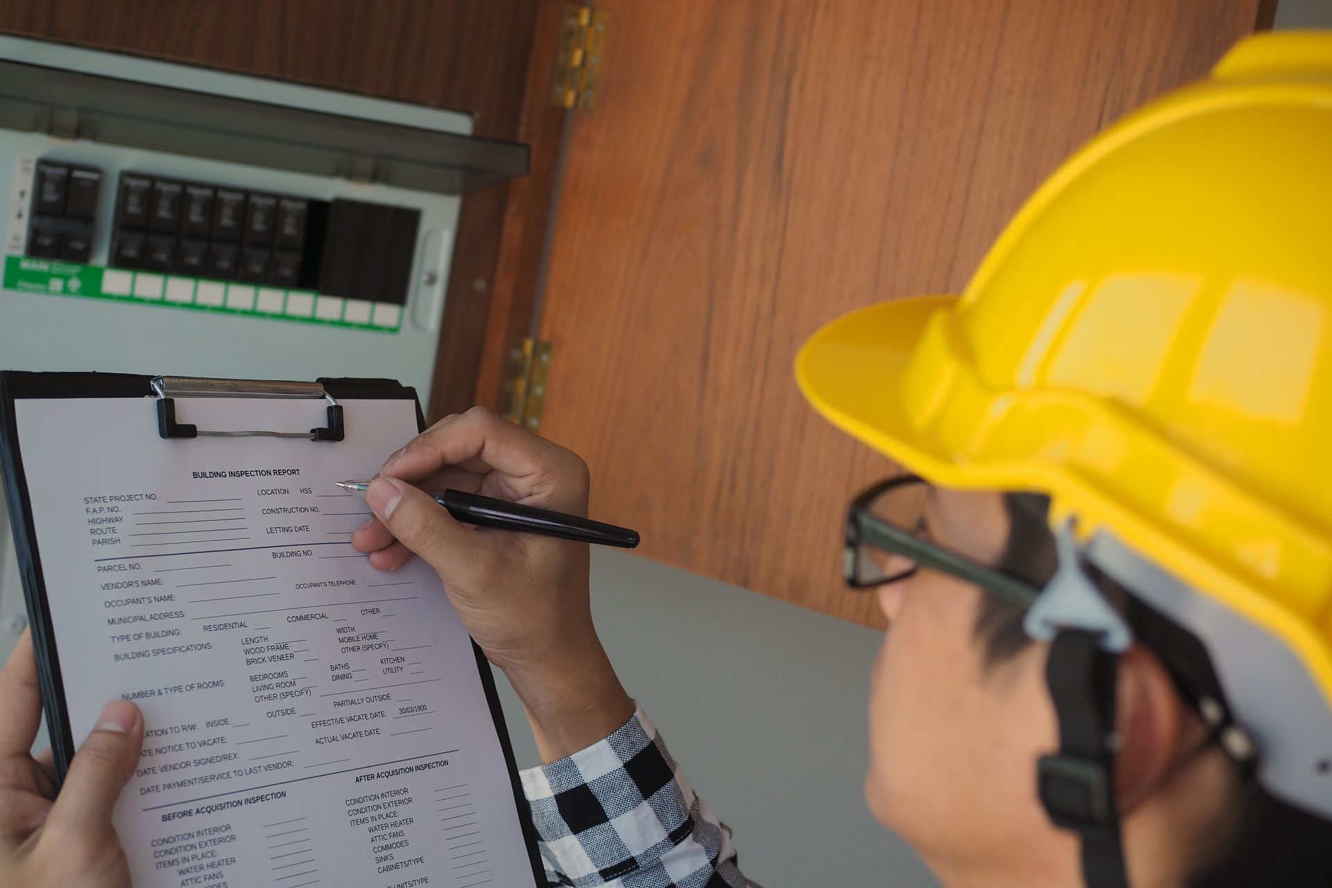 A man wearing a hard hat is writing on a clipboard.