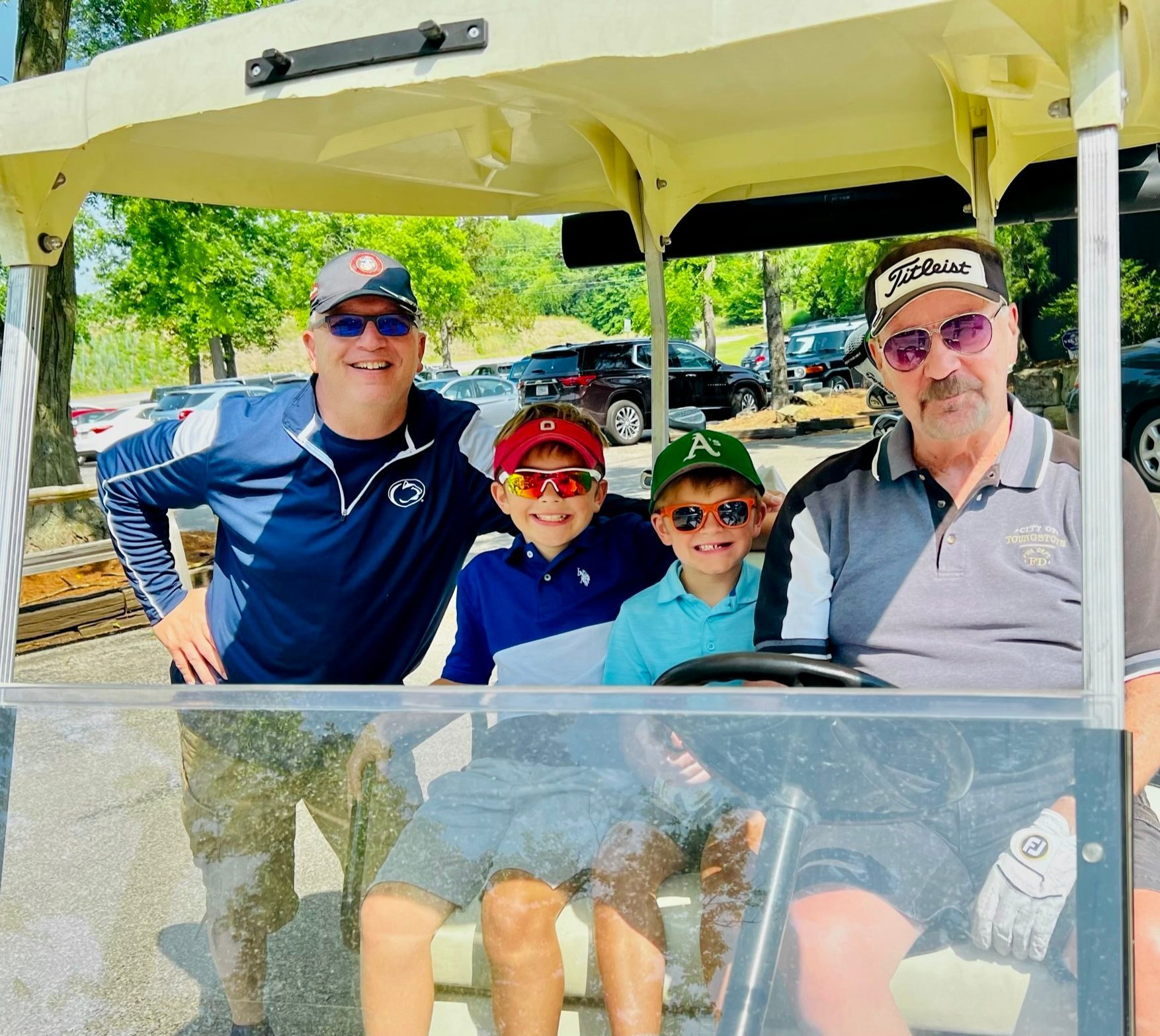 Four people in a golf cart: two adults and two children; smiling at the camera outdoors.