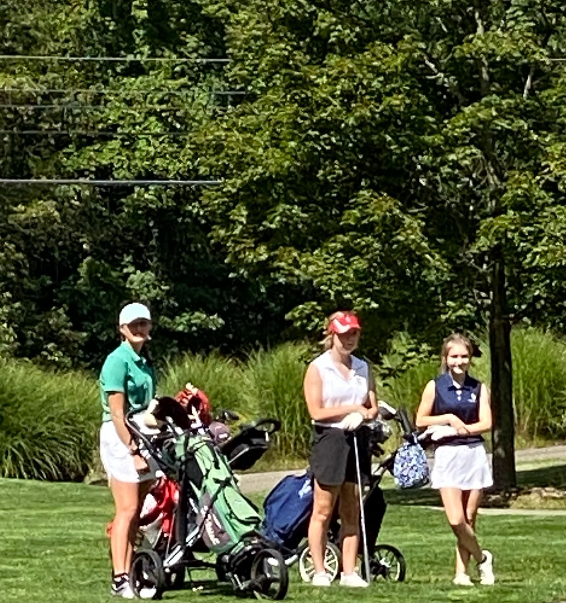 Three golfers standing on a green, next to golf bags, under a sunny sky.