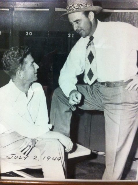 Two men in a locker room, one seated, the other leaning, speaking, dated July 2, 1949.