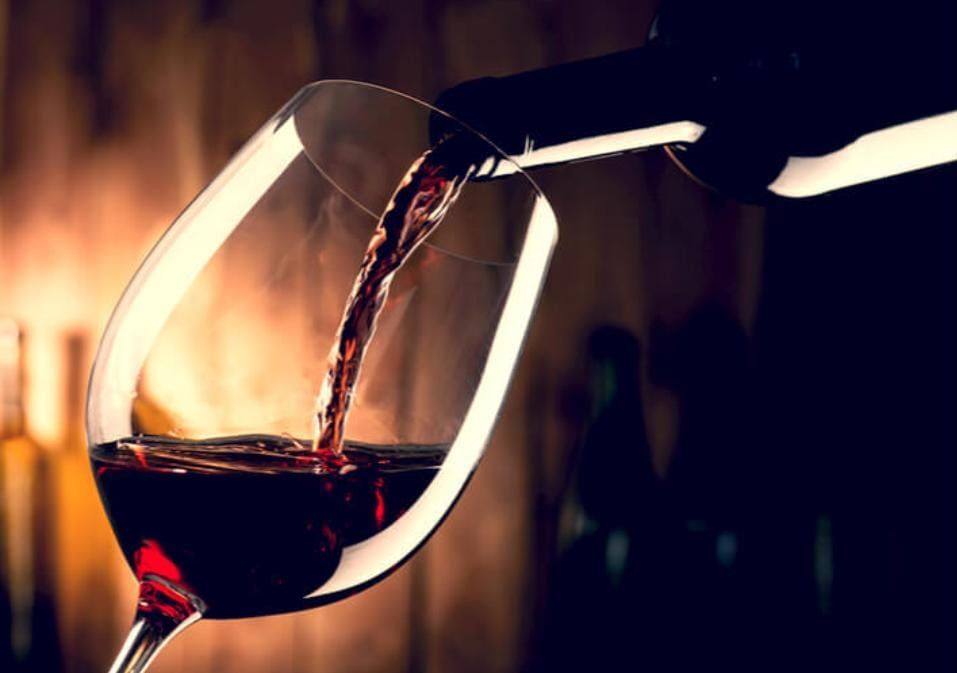 Vino tinto vertido desde una botella a una copa contra un fondo borroso.