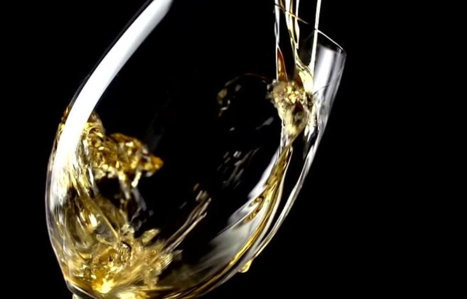 Vino blanco vertido en una copa sobre un fondo negro.