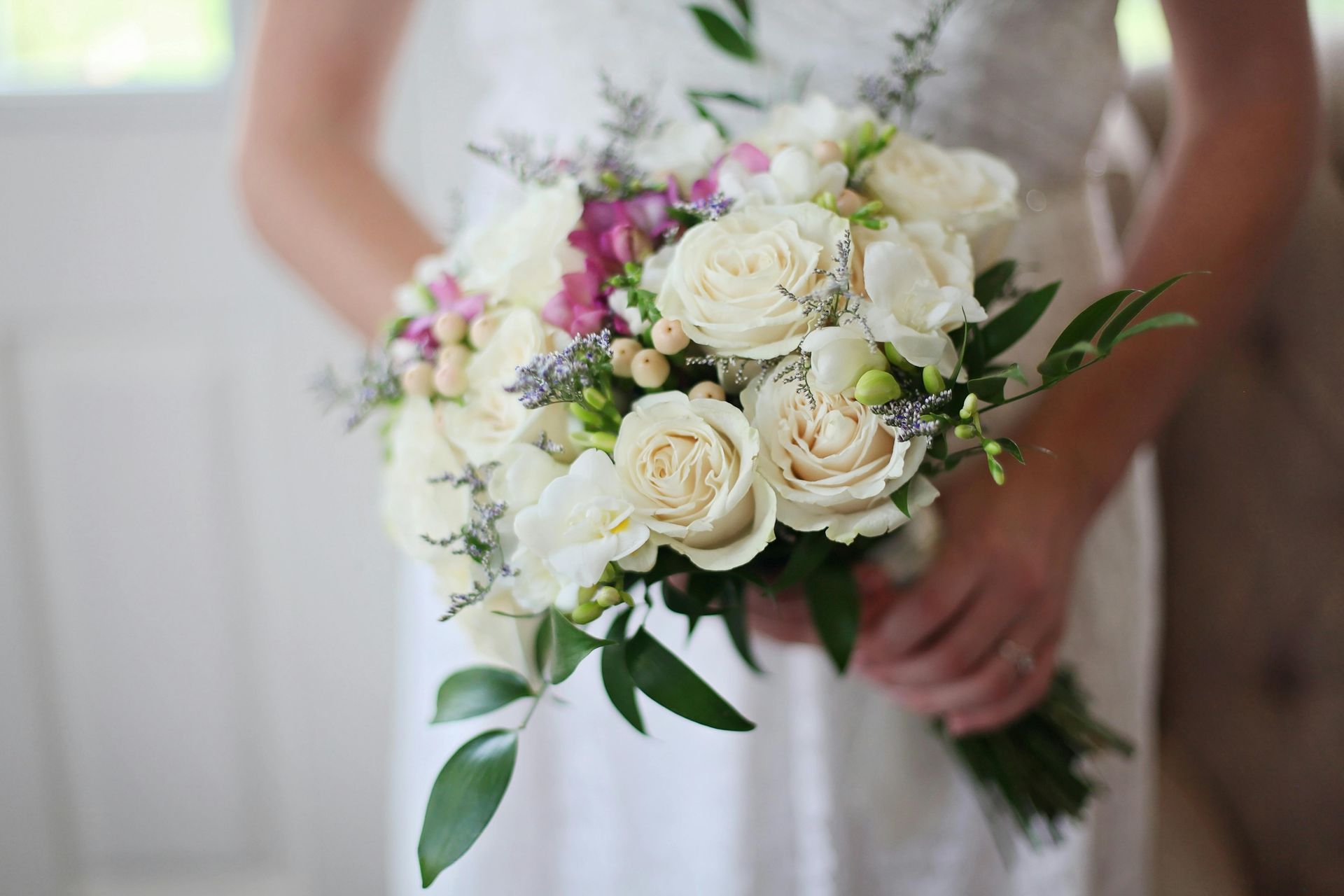 Bride holding a bouquet of white roses, purple flowers, and green foliage.