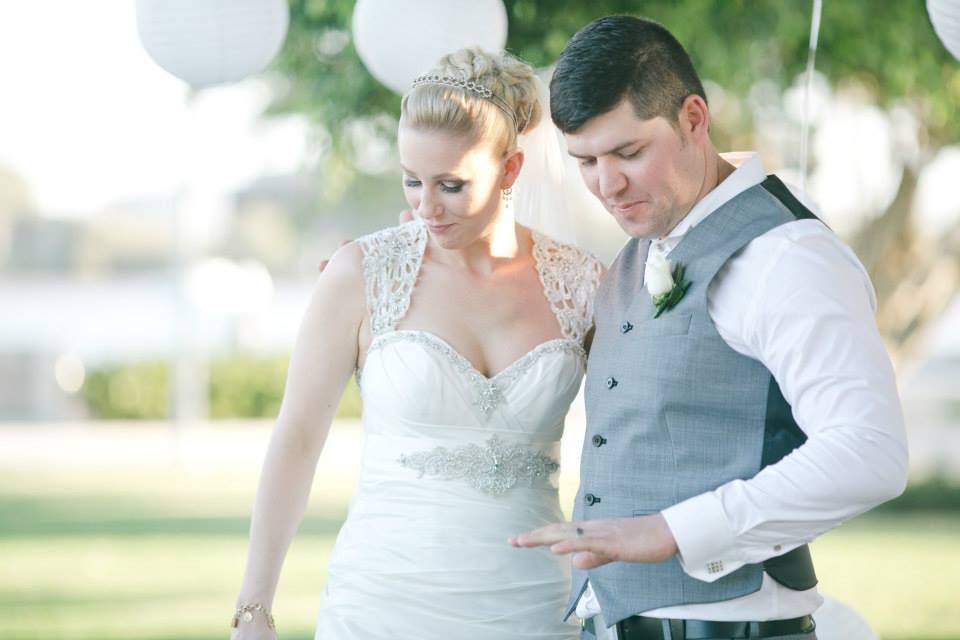 Bride and groom looking at wedding ring outdoors. The bride wears a white dress and the groom a gray vest.