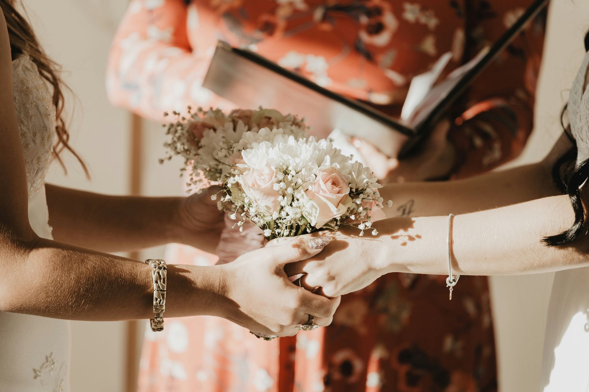Two people holding hands over a bouquet, during a wedding ceremony.