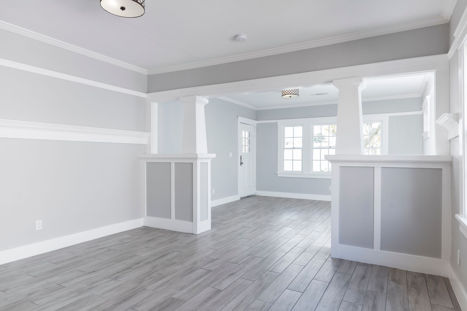 Empty light-gray living room with white trim, wood floors, and a bright windowed alcove