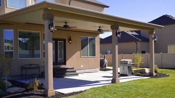 Covered patio with concrete flooring, columns, and outdoor grill.