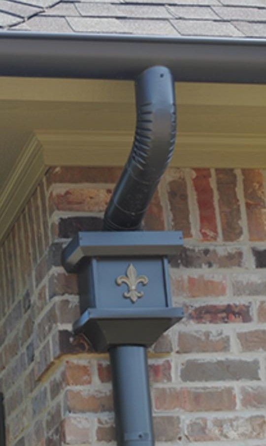 Gray downspout with fleur-de-lis detail on a brick building.