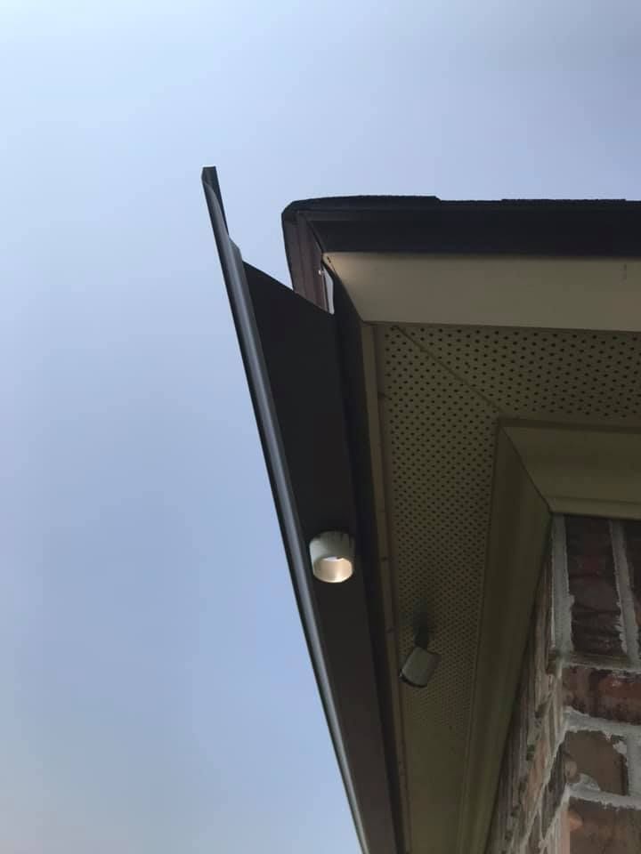Brown gutter extends from the roofline of a brick building, with a security camera visible.