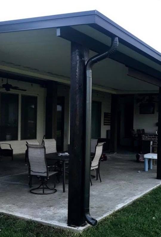 Covered patio with black support beams, furniture, and a gutter.