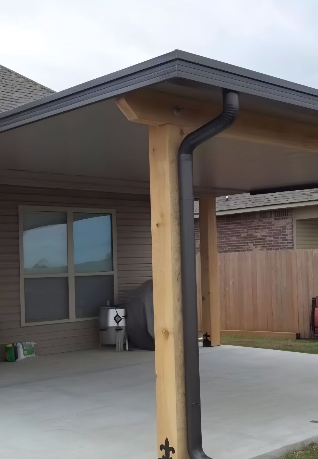 Covered patio with dark gutters, wooden beams, and concrete floor. Building in background.