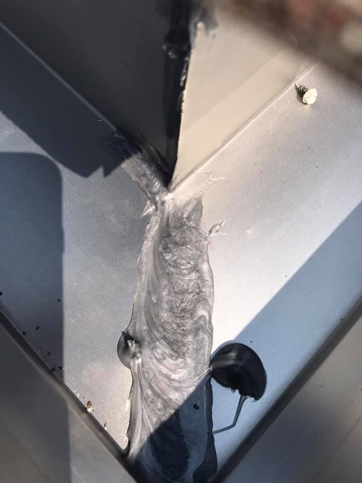 Silver metal corner filled with thick, textured, dark gray sealant.