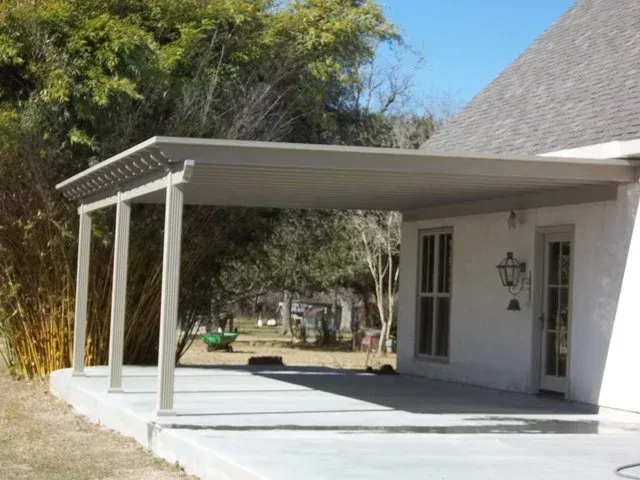 Beige patio cover extending from a white house with concrete patio.